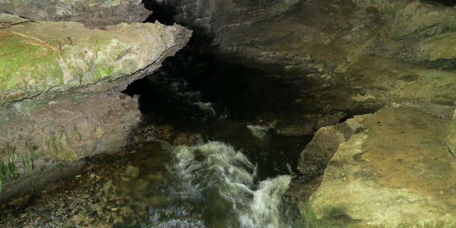 Photograph of small river flowing out of cave mouth.