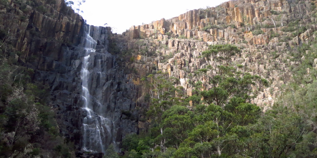 Photograph of long brown cliff with waterfall flowing down part of it.